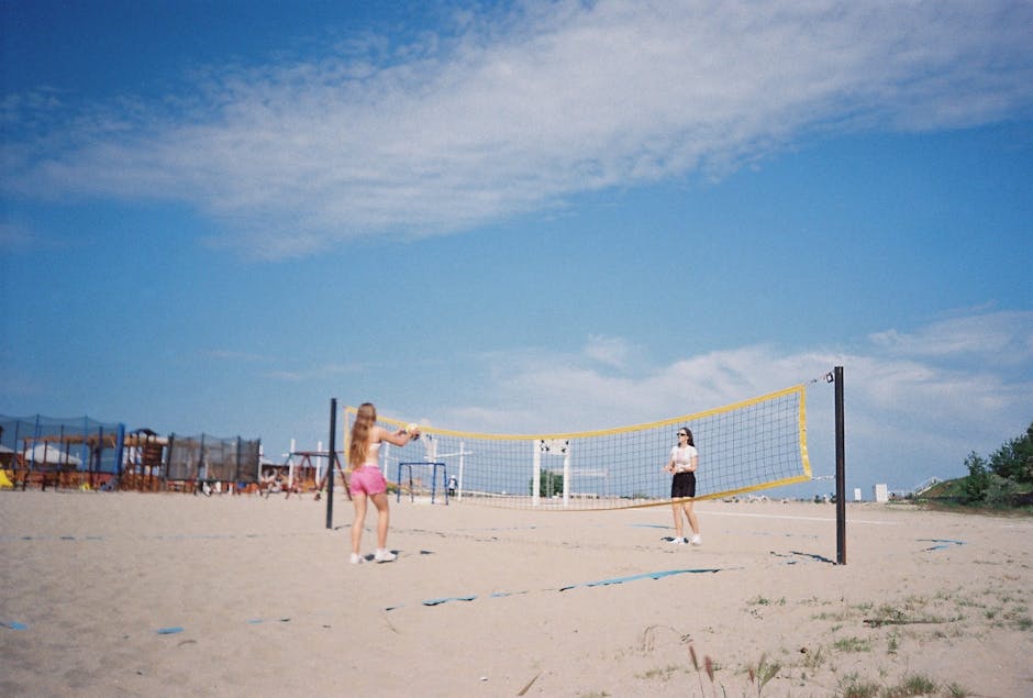 Two young girls enjoy a game of beach volleyball under clear blue skies.