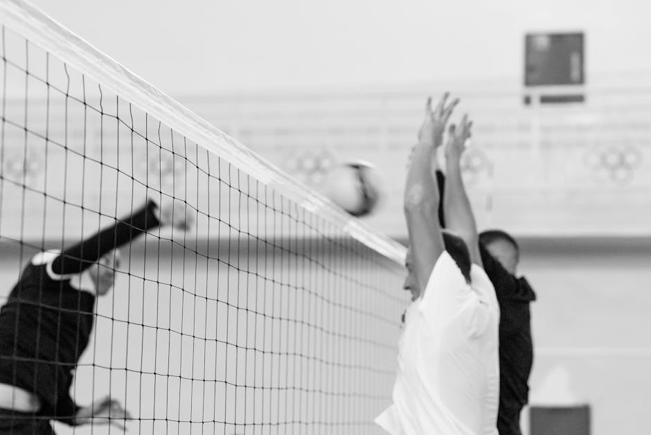 Black and white photo capturing players in mid-air blocking shot at volleyball net.