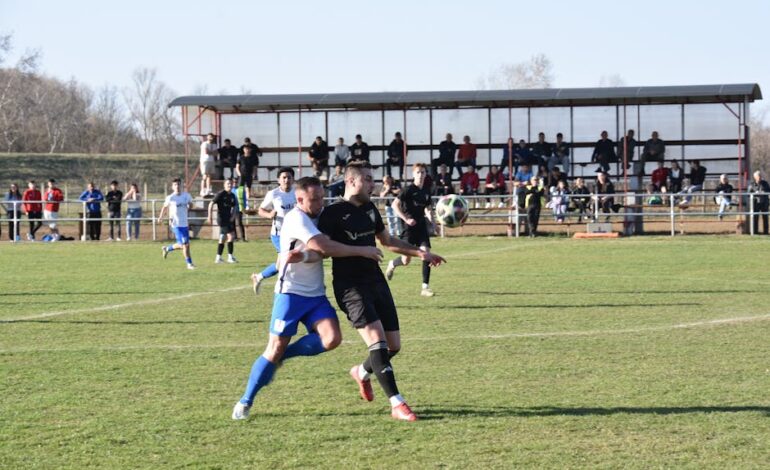 Soccer players in action on a sunny day in Vásárosnamény, Hungary with spectators watching.
