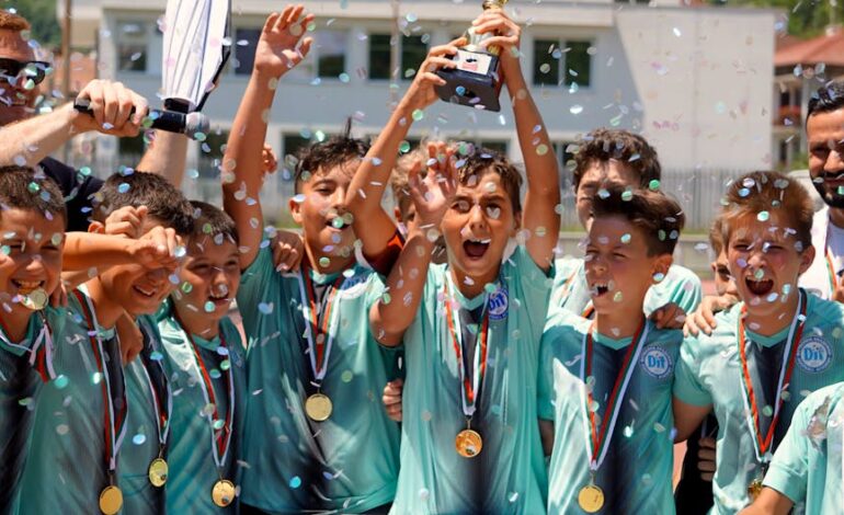 Group of boys celebrating a soccer tournament victory with confetti and trophy.