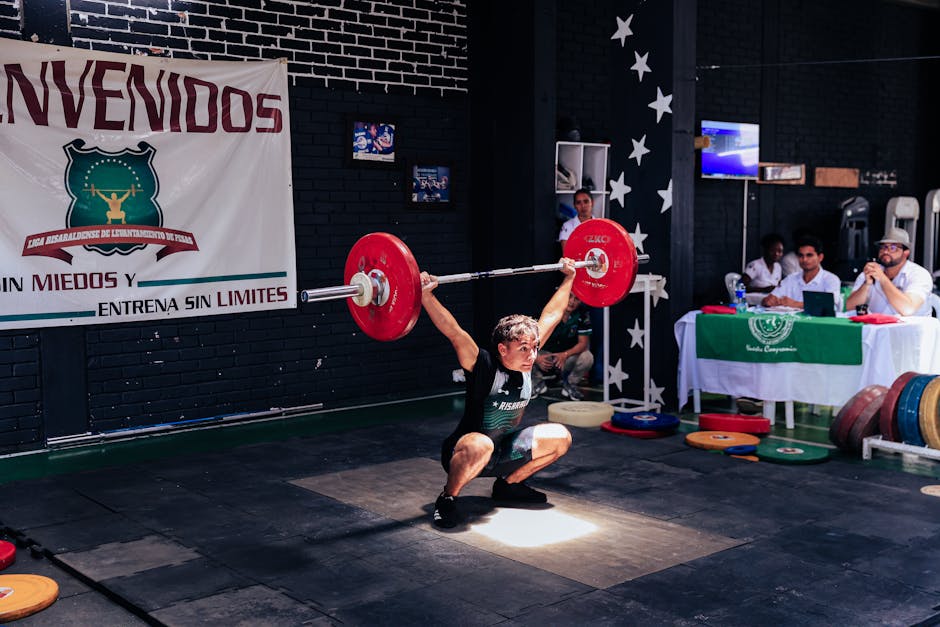 Athlete executing a snatch lift at a weightlifting competition indoors.