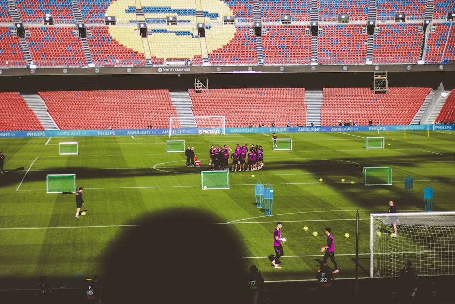 Football team training in a large empty stadium with vibrant red and blue seats.