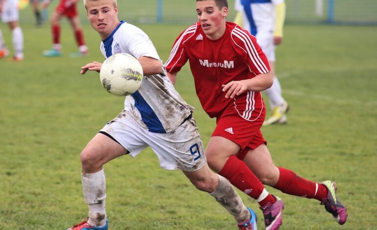 Two teenage soccer players competing fiercely on a muddy grass field.