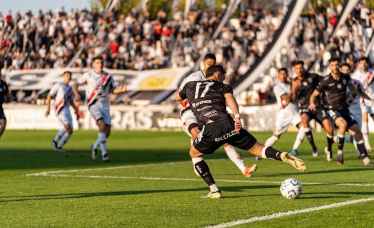 A dynamic football match with players in motion on a sunny day, witnessed by a packed stadium.