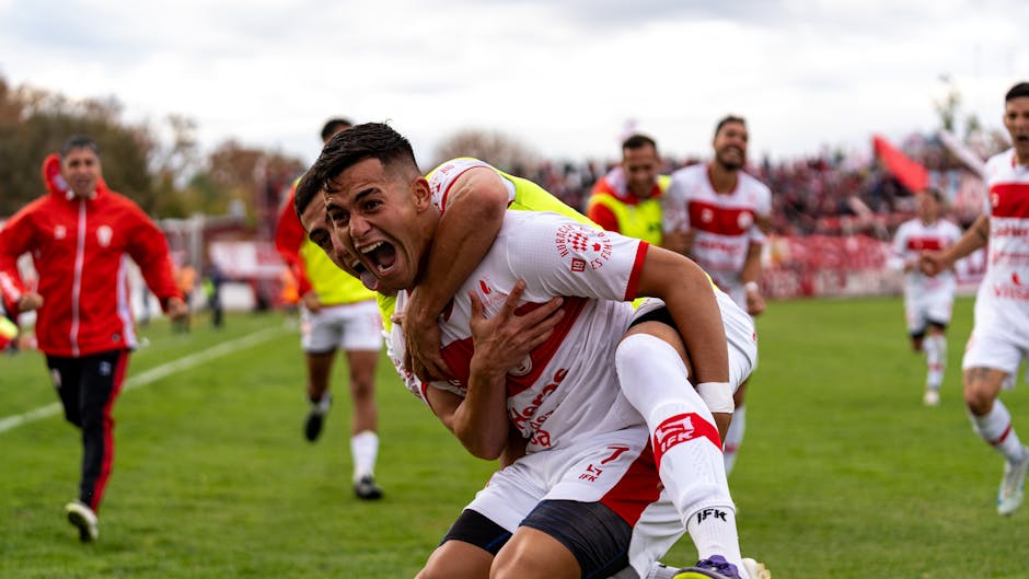 Group of soccer players joyfully celebrating a win on a grassy field.
