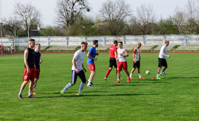 A group of young male athletes practicing soccer on an outdoor field on a sunny day.