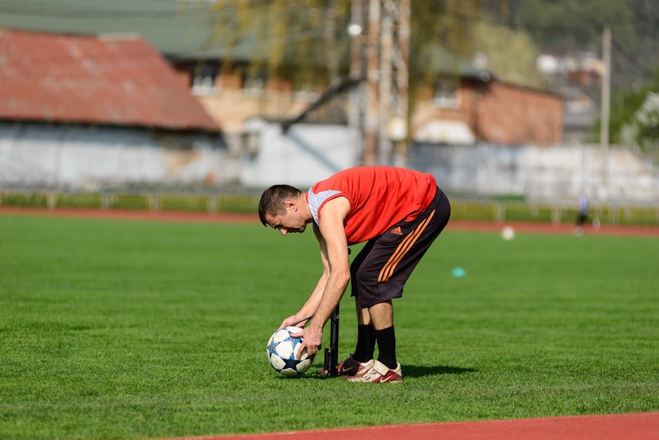 An athlete in sportswear preparing a soccer ball on a grass field during daytime training.