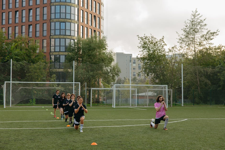 A group of kids performing warm-up exercises with their coach on a soccer field.