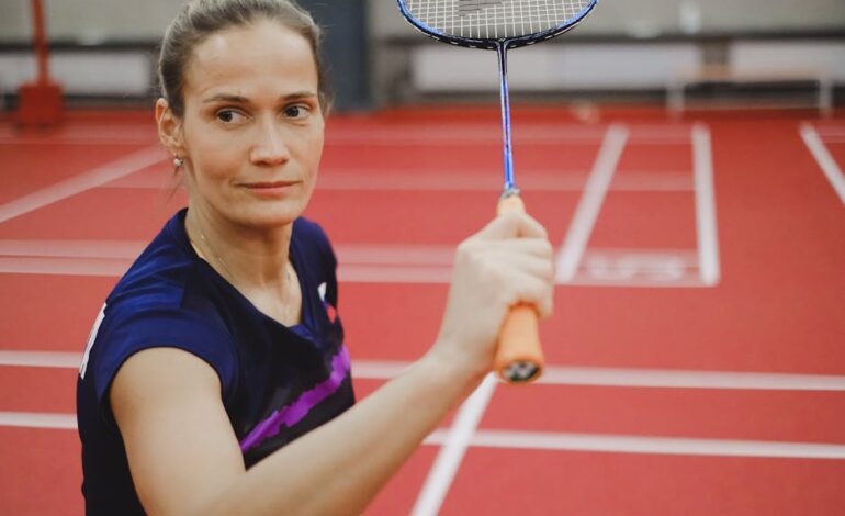 Focused female badminton player ready to hit, on a vibrant red indoor court.