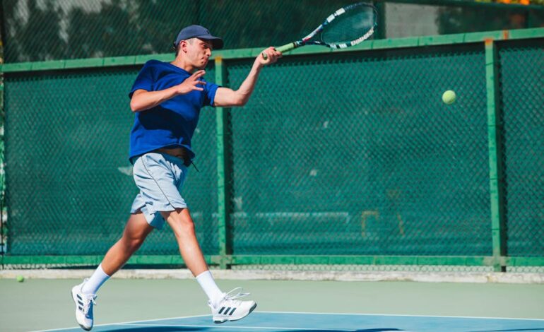 A young male tennis player in mid-swing during a sunny match on an outdoor court in Mexico.