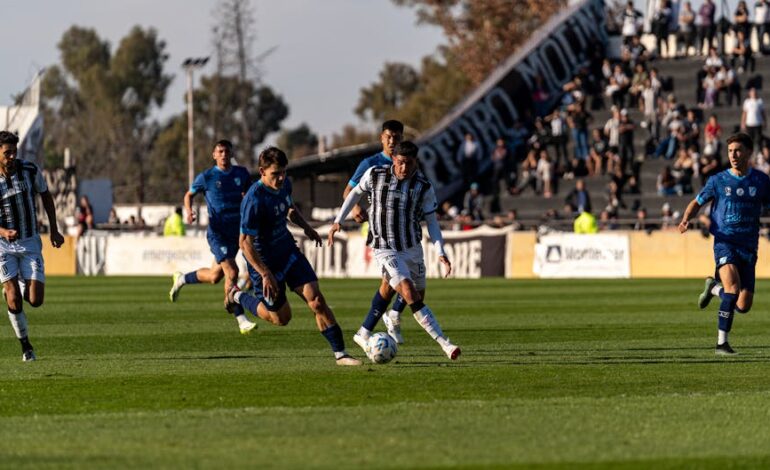 Football players in action during a sunny outdoor match with a vibrant crowd.