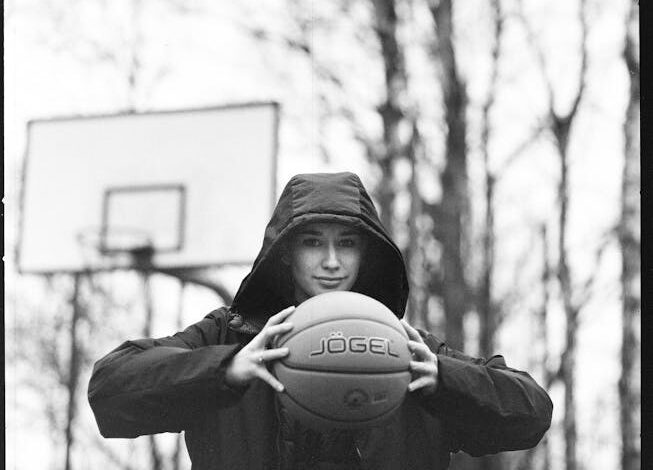 Black and white image of person holding basketball outdoors in winter.