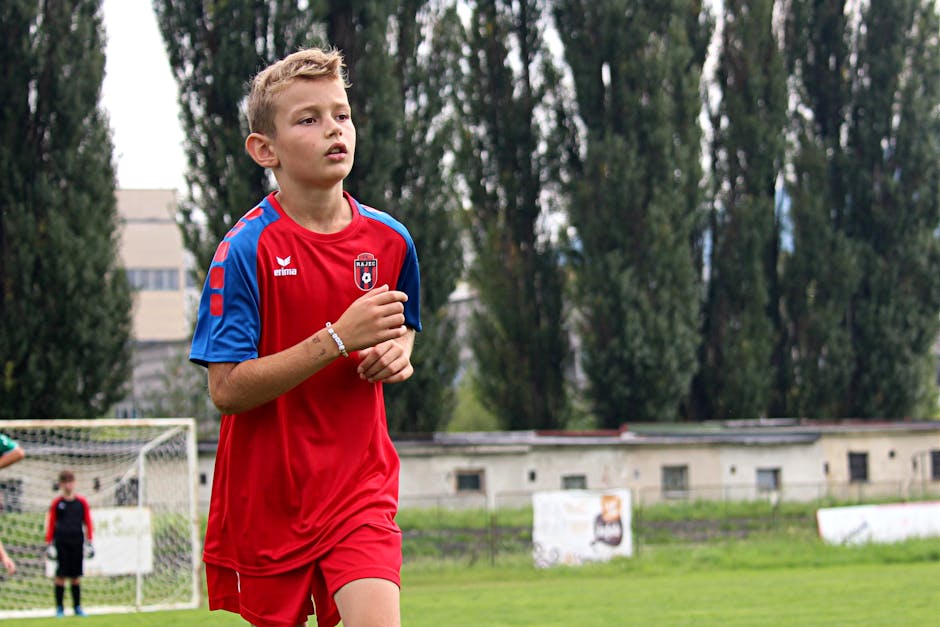 A young soccer player in a red uniform focuses during a game on an outdoor field.
