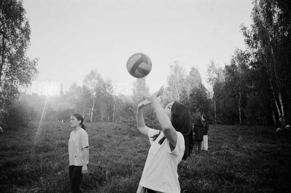 Women enjoy a casual volleyball game outdoors in a park setting, captured in black and white.