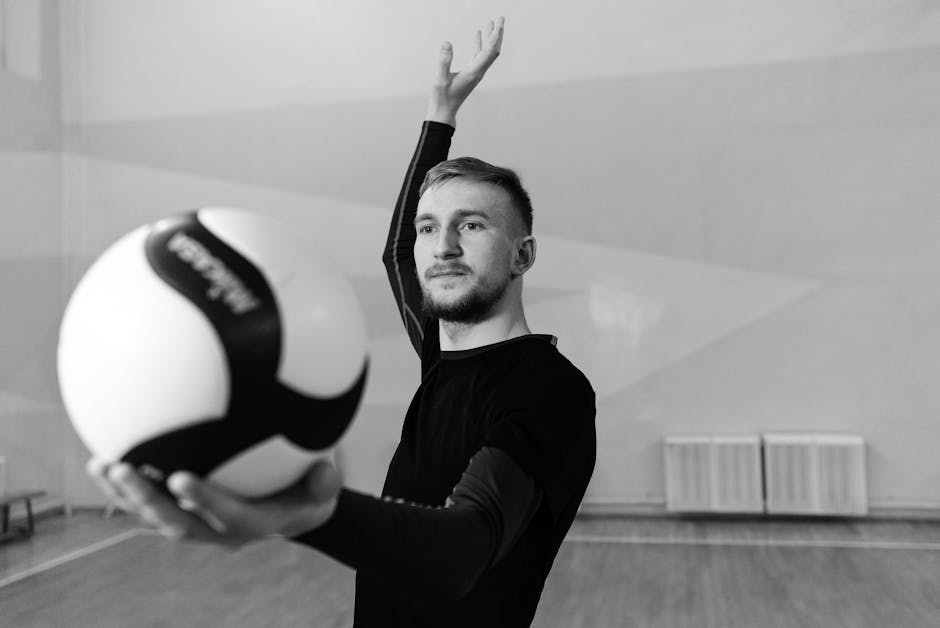 Black and white photo of a male volleyball player poised with the ball indoors.