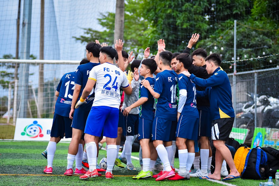 A soccer team in a group huddle on a grassy football field in Hanoi, Vietnam.