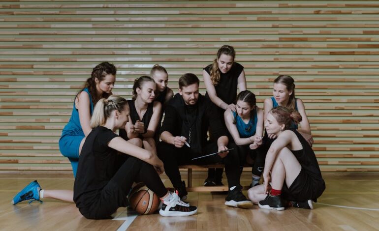 A coach strategizes with a women's basketball team in a gymnasium.