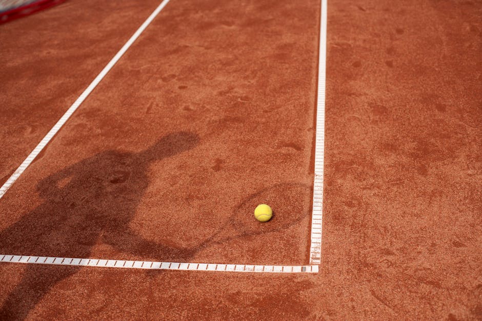 Shadow of a tennis player on a clay court with a yellow tennis ball. Perfect for sports and tennis themes.