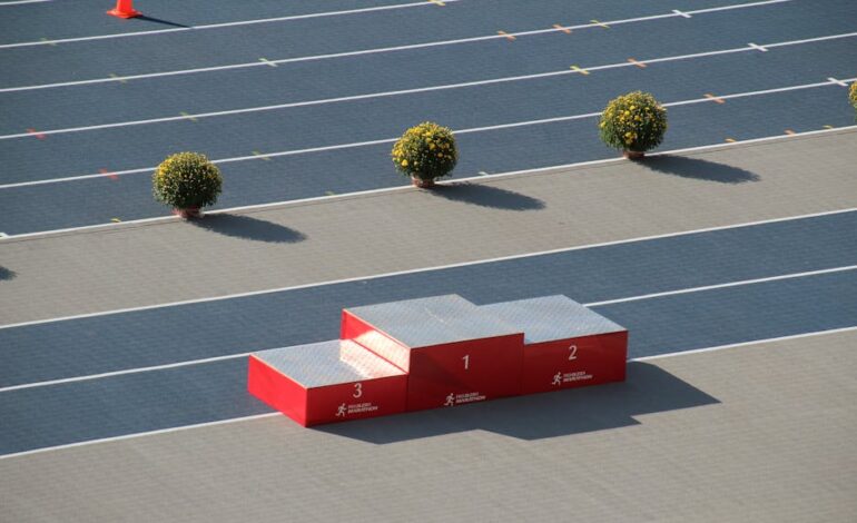 Red podium on a sunny outdoor athletics track with decorative plants.