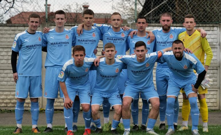 Group portrait of an amateur football team posing outdoors in blue jerseys.
