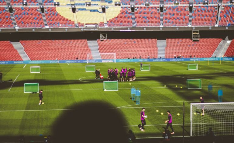 Football team training in a large empty stadium with vibrant red and blue seats.