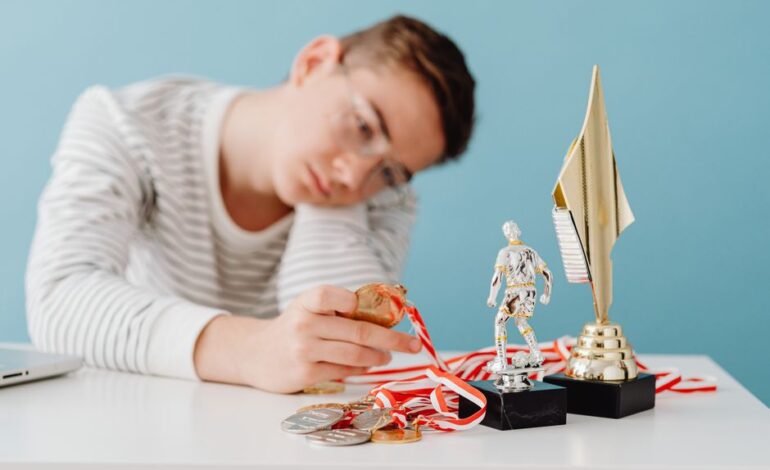 A thoughtful teenager sits by a table with various trophies and medals.