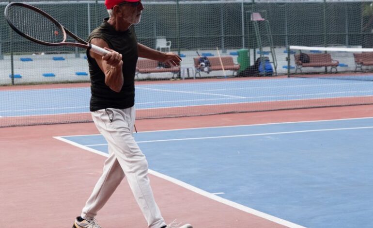 Elderly man playing tennis on a sunny outdoor court, displaying energy and passion.