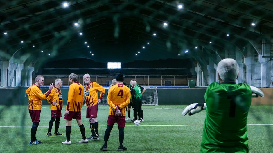 Senior adult football team playing indoor match in Wakefield, England. Team strategy discussion on the pitch.