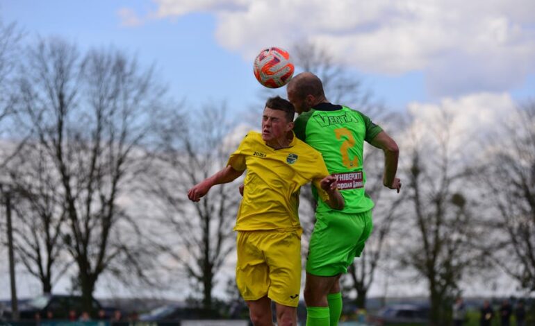 Two soccer players compete for the ball in midair during an outdoor match.