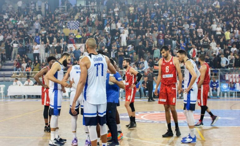 Basketball players in action during a competitive match with a full stadium crowd.