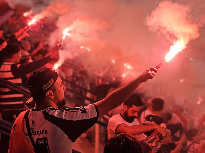 Energetic crowd celebrating with red flares at a sports event, creating a vibrant and passionate atmosphere.