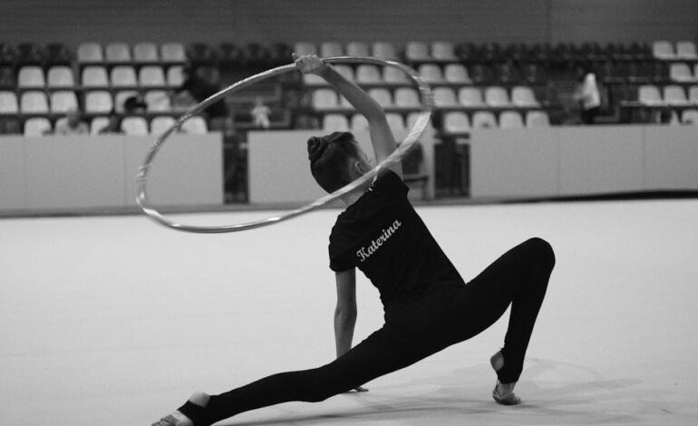 Gymnast in flexible pose with hoop in an indoor arena.