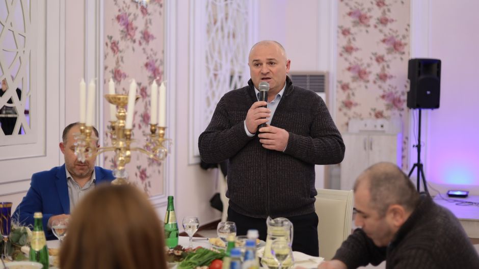 A man speaking into a microphone during a formal dinner gathering indoors with elegant decor.
