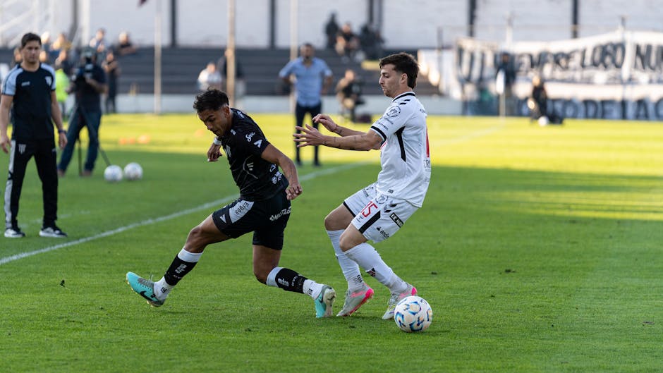 Intense action between two footballers competing in an outdoor match with clear daylight.