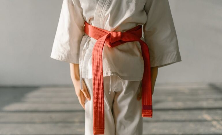 Close-up of a martial artist wearing an orange belt and white uniform, standing indoors.