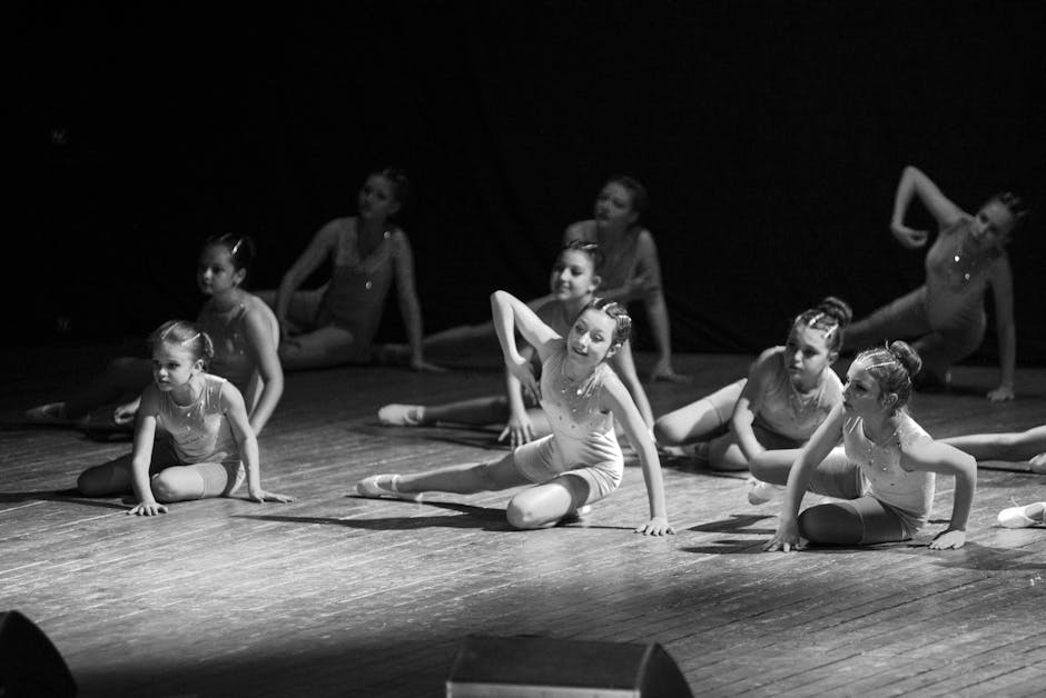 Young ballerinas performing a choreography on stage in a monochrome setting.