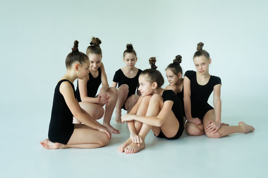 Group of six young ballerinas in black leotards relaxing on the studio floor.