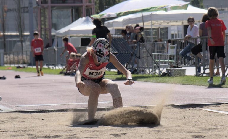 Female athlete captured mid-landing in the long jump event during a sunny sports meet.