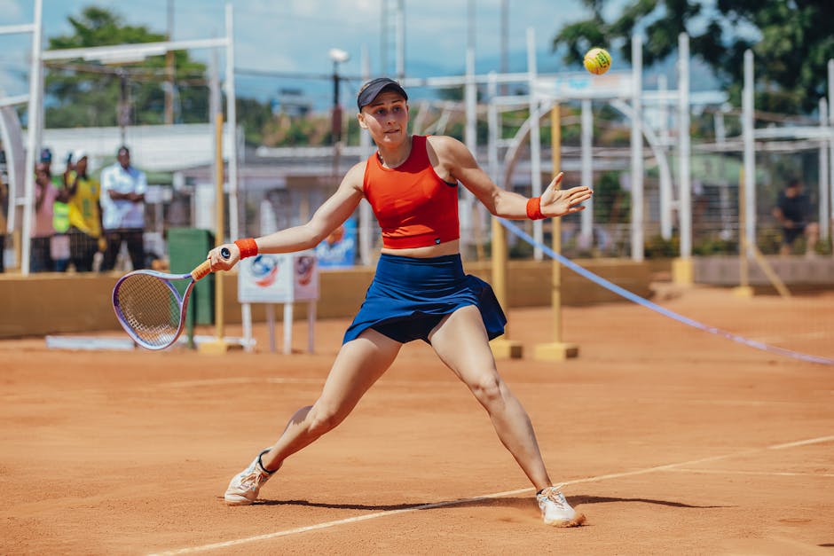 Dynamic shot of a female tennis player hitting a forehand on a clay court during a sunny day.