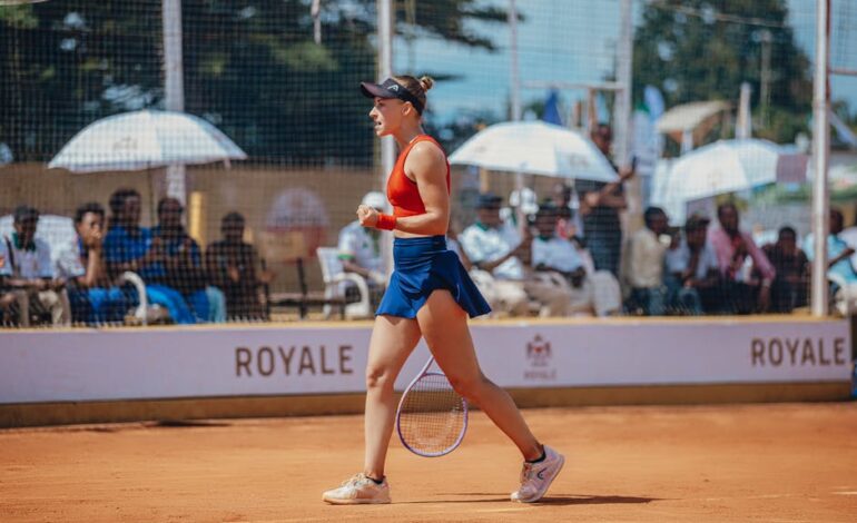 A triumphant female tennis player in action on a clay court with spectators in the background.