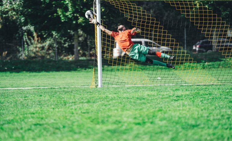 Goalkeeper leaping to save a soccer ball during an outdoor match.