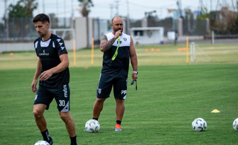 Focused soccer coach instructing players during a training session on a green field.