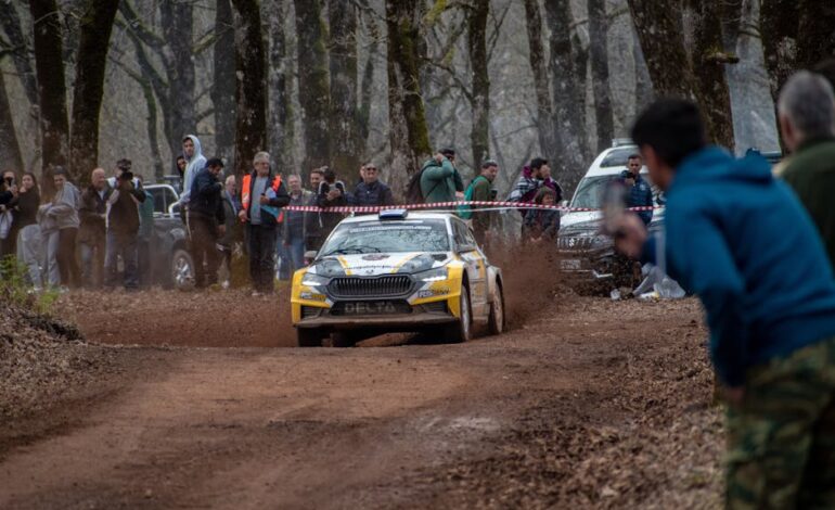 Exciting rally car event with spectators on a dirt track in Ilia, Greece, showcasing motorsport action.
