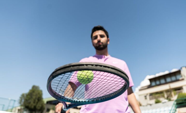 Low-angle shot of a tennis player holding a racket with a ball against a clear blue sky.