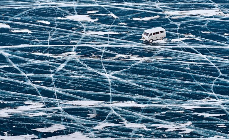 A van driving across the icy surface of Lake Baikal with intricate ice patterns.