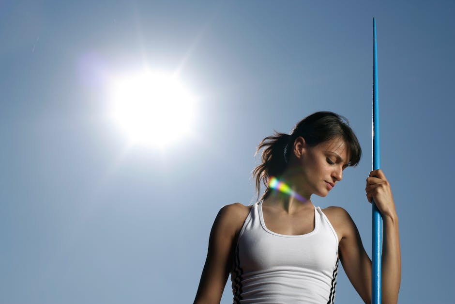 Woman athlete with javelin against a sunny sky, showcasing strength and focus.