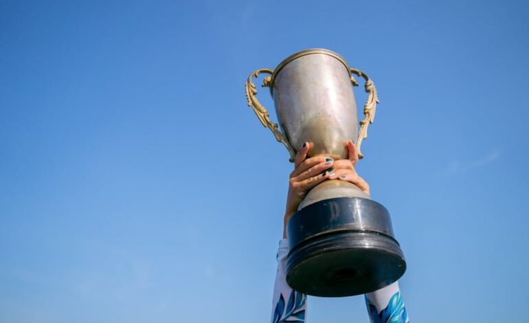 Hands holding a trophy high against a clear blue sky, symbolizing victory and success.