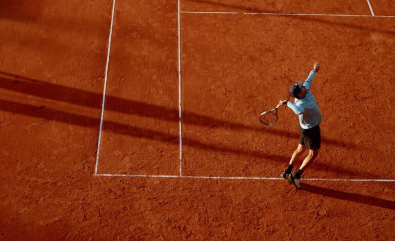A dynamic shot of a tennis player serving on a clay court during sunset.