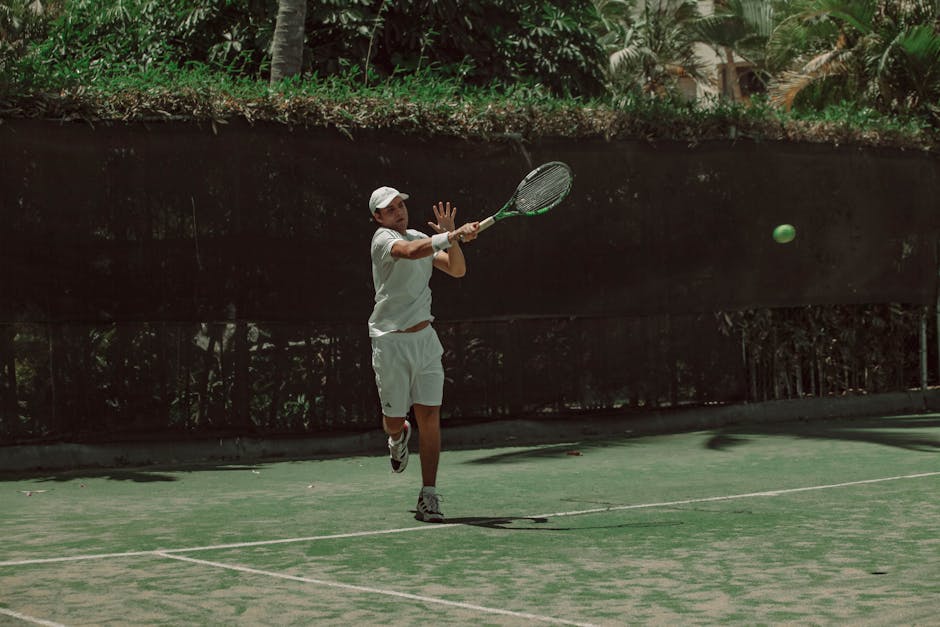 Male tennis player hitting a forehand shot on an outdoor court during a sunny day.