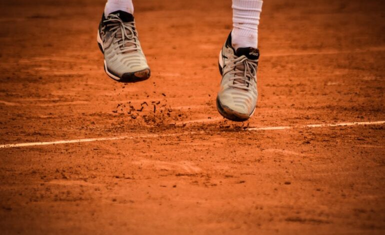 Close-up of an athlete's shoes mid-jump on a clay tennis court.